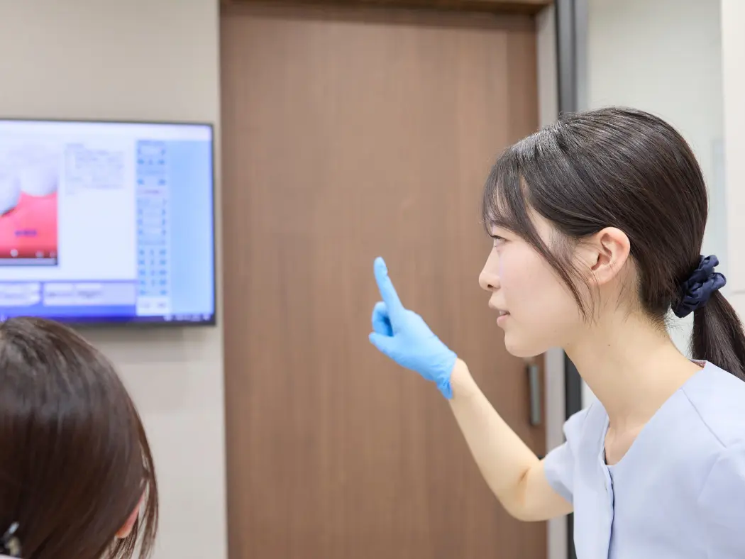 口腔内スキャナーのモニターを患者さんに見せながら説明しているカット。患者さんが画面に見入っている自然な表情。モニターに口腔内画像が映っていると説得力が増す。