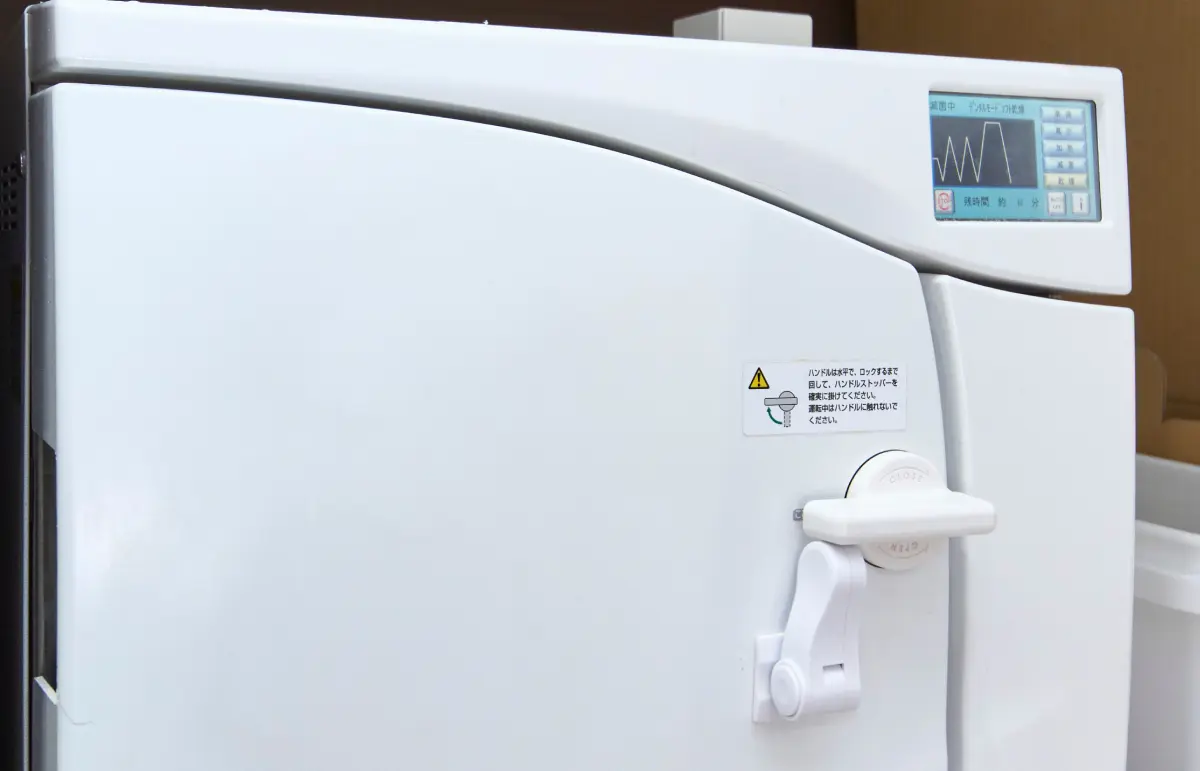 クラスB滅菌器が稼働中のランプを灯している全体像。清潔感のある滅菌コーナーの空間。設備の先にある「スタッフの快適さ」が主役となる構図。