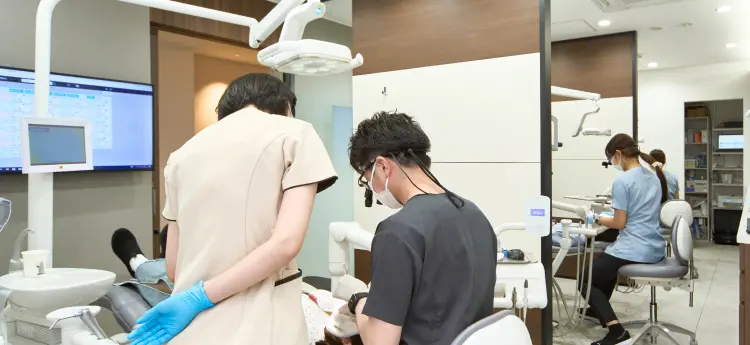 診療室の全景。手前ではルーペを装着したスタッフが診療にあたり、奥のユニットでは水色のスクラブを着た歯科衛生士が患者さんの処置を行っている