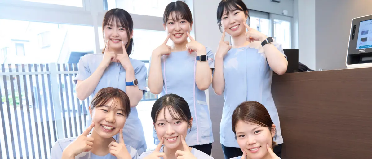 ひすい歯科のスタッフ全員が診療室の外で自然な笑顔で並んでいる集合写真。白衣と明るい空が印象的